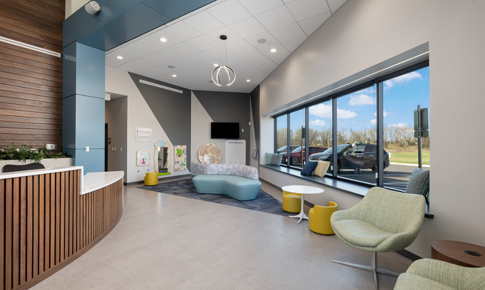 Bright children's lounge with colorful seating, wall activity toys, and large windows overlooking parking lot
