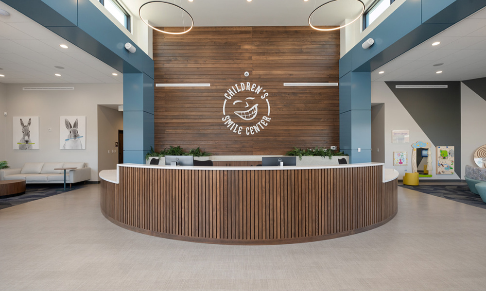 Bright, modern Children's Smile Center lobby with curved wood reception desk and logo accent wall